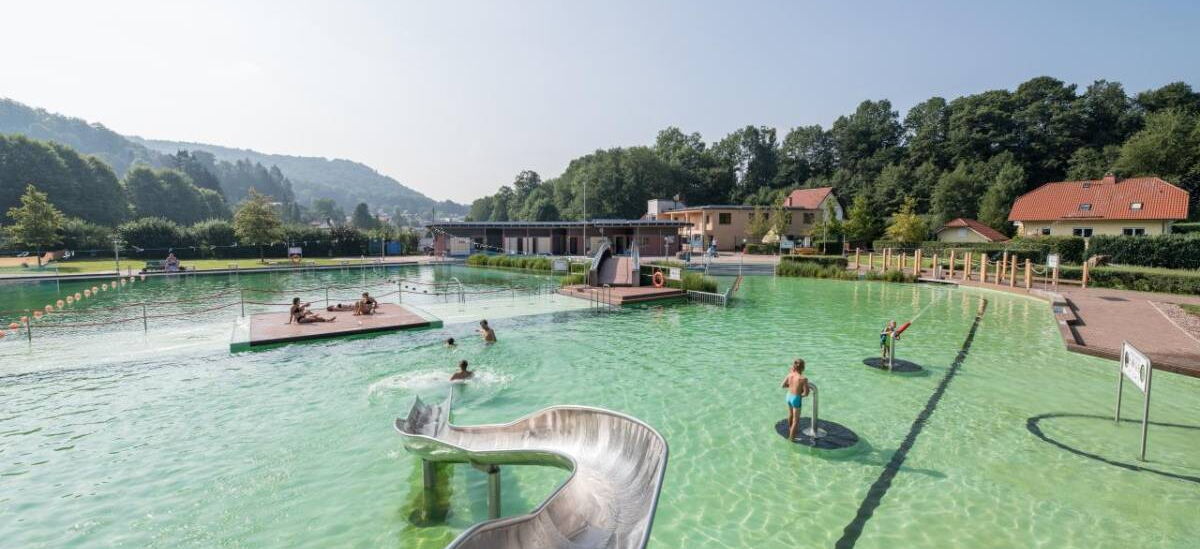 Aufnahme des Freibades BioBad Glücksbrunn mit Wasserrutsche, Wasserkanonen, und Liegeflächen