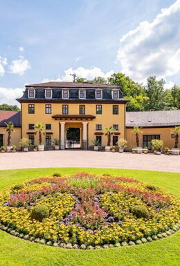 Landschaftsaufnahme mit Hofmarschallamt und kleinem bepflanzten Teppichbeet im Schlosspark Altenstein